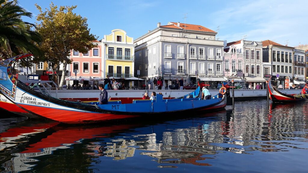 Several Moliceiros boats on a river, with colorful houses behind them. Image: LuisPinheiro1945